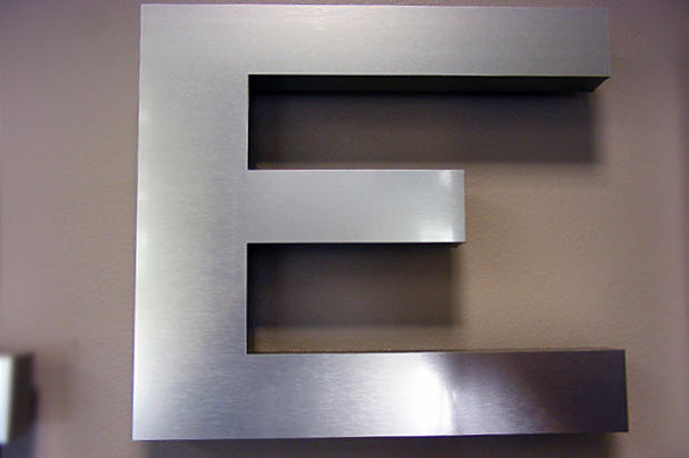 Dimensional brushed metal office sign installed on an interior wall
