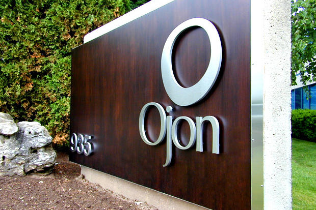 Dimensional brushed metal letter sign on wooden panel mounted to a concrete pylon