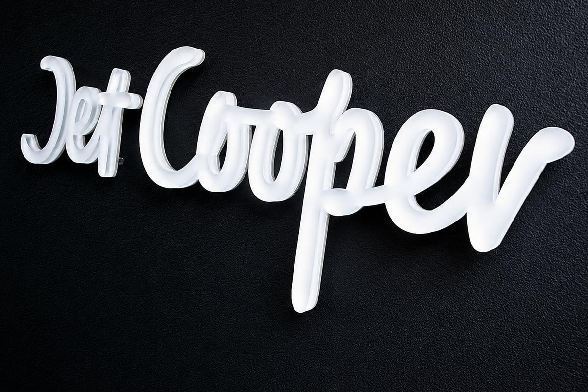 Close-up of a pastel ice-white frosted acrylic Jet Cooper script logo mounted on a textured black office wall.